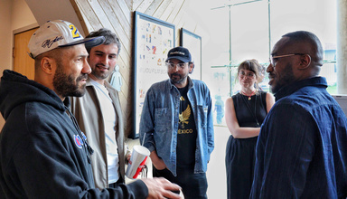 Five people, including filmmaker Khalik Allah, Laura Gede, and Jacob Kessler, stand in conversation in a bright lobby space during an Iowa City Documentary Film Festival event, with film posters visible on the wall behind them.