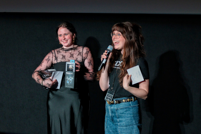 Cinematic Arts professor and ICDOCS director, Laura Gede, and a student speak at the Iowa City Documentary Film Festival against a black background.